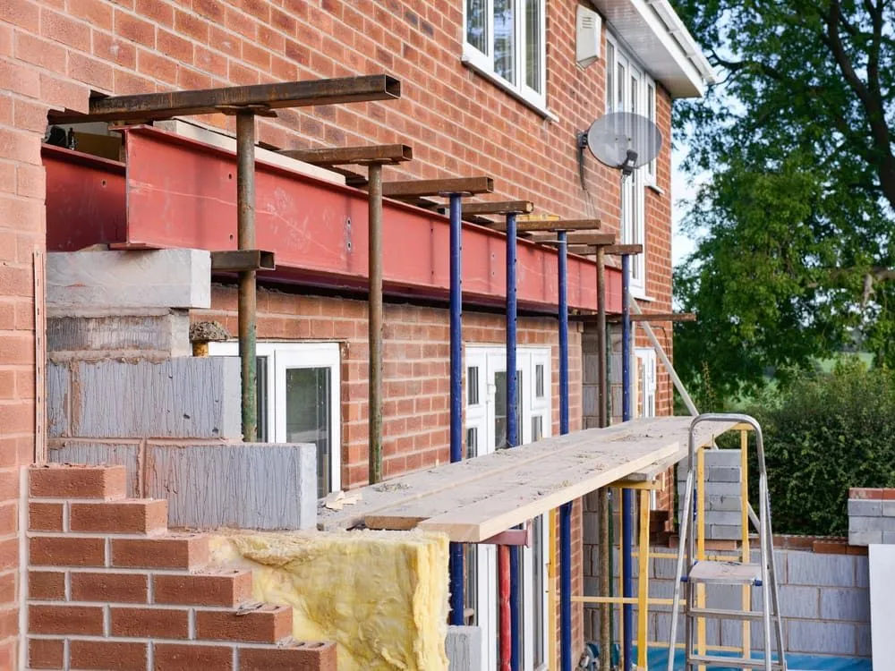 A Brick House is Being Remodeled With Scaffolding and a Ladder — Ozi Construction Pty Ltd in Bondi, NSW