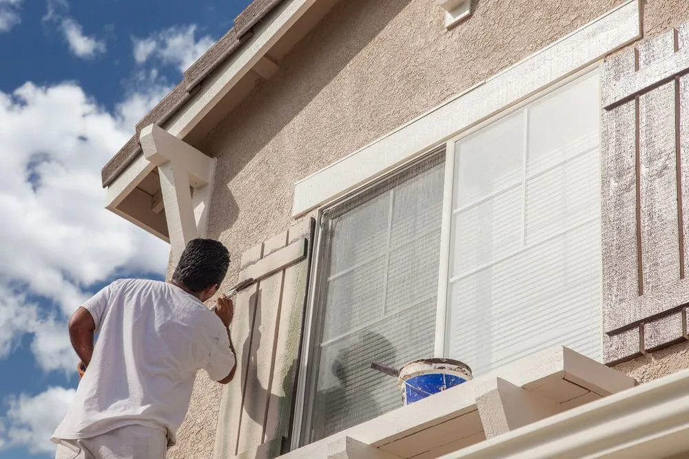 A Man is Painting a Window on the Side of a House — Ozi Construction Pty Ltd in Bondi, NSW