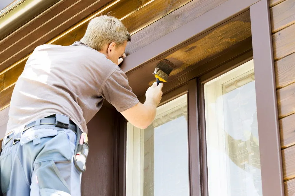 A Man is Painting a Window Frame With a Brush — Ozi Construction Pty Ltd in Chatswood, NSW