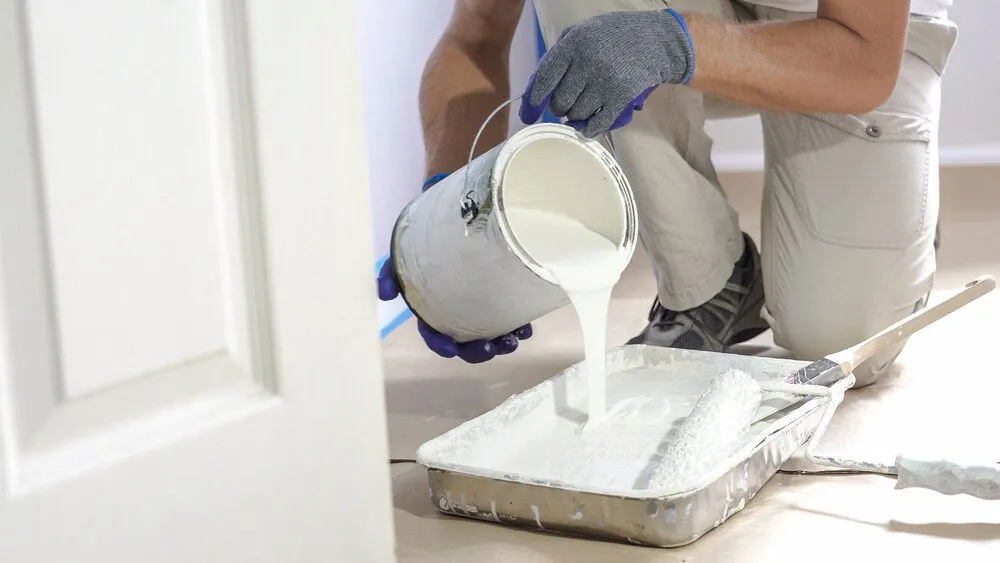A Man is Pouring White Paint Into a Tray — Ozi Construction Pty Ltd in Sydney, NSW